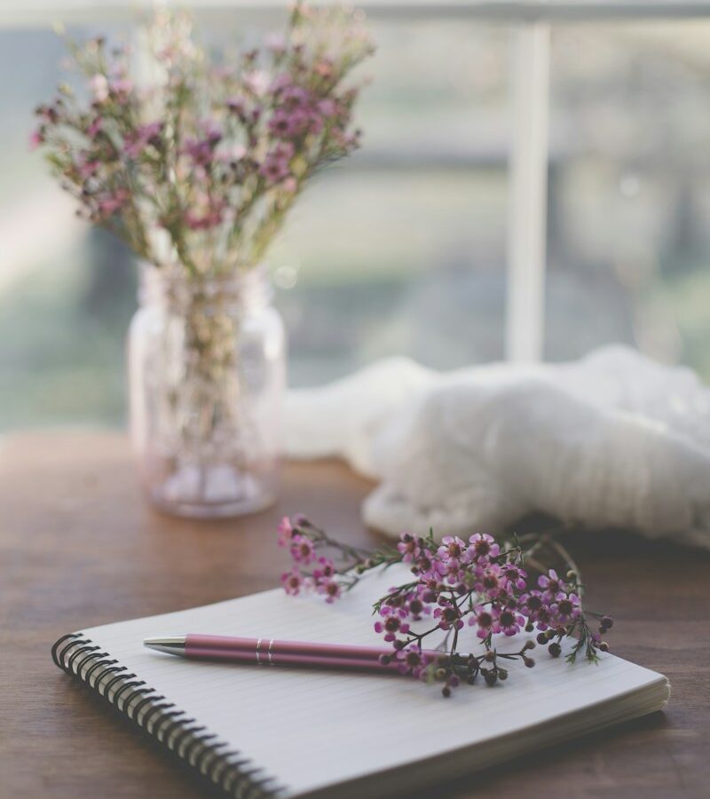 Cuaderno y flores secas sobre una mesa junto a una ventana
